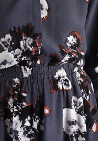 Abito floreale caratterizzato da un tessuto grigio scuro con motivi floreali bianchi e rossi, vita elasticizzata e una texture fluida.