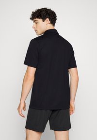 Fekete pólóing, sima anyagból készült, rövid gallérral és rövid ujjakkal, szürke sorttal párosítva. A háta sima, mintázat nélkül.