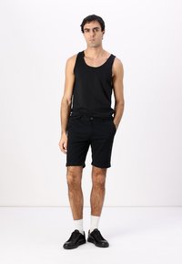 Top de tirantes de algodón negro y pantalones cortos. Los pantalones cortos tienen un cierre de botón, y el conjunto se complementa con zapatillas negras y calcetines blancos tipo crew.