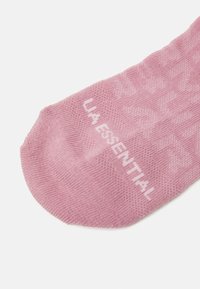 Rosa strikket sokk med teksturert mønster og subtil merking "LA ESSENTIAL" i hvitt, med rund tå og ribbestrikket mansjett.