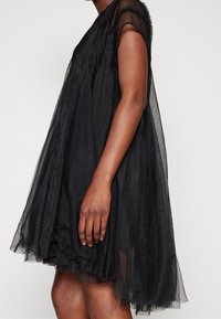 Czarna sukienka z tiulu z krótkimi rękawami, warstwowym krojem i luźnym fasonem. Posiada teksturowany materiał z delikatnym drapowaniem i przezroczystym wykończeniem.
