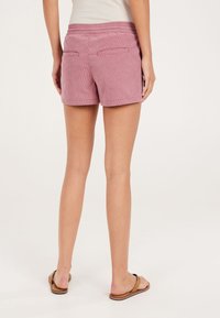 Różowe sztruksowe szorty o gładkiej fakturze, wyposażone w dwie tylne kieszenie oraz wygodną elastyczną talię. Długość casual, odpowiednia na ciepłe dni.