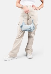 Sac à main en tissu bleu clair avec un design courbé, deux poches extérieures et une courte bandoulière, avec des accents en métal argenté.