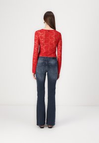 Top de encaje rojo de manga larga con un diseño ajustado, combinado con jeans acampanados de color azul oscuro que cuentan con bolsillos traseros y una textura de denim clásica.
