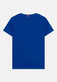 Modré bavlněné tričko s krátkým rukávem a kulatým výstřihem. Na zadní straně se nachází červený a bílý pruhovaný štítek. Hladká textura, bez vzorů.