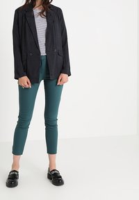 Svart kavaj med texturerad tyg, kombinerad med en randig topp och smala byxor i teal. Skorna har en kraftig sula med kedjedetalj.