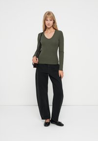Olijfgroen lang overhemd met een ronde hals, gecombineerd met hoge zwarte wijde broek en zwarte platte schoenen.