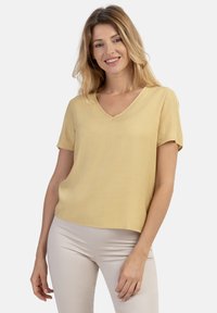 Kortærmet bluse med v-hals i lys gul, lavet af et glat stof med løs pasform, der har en lige kant og minimal dekor.