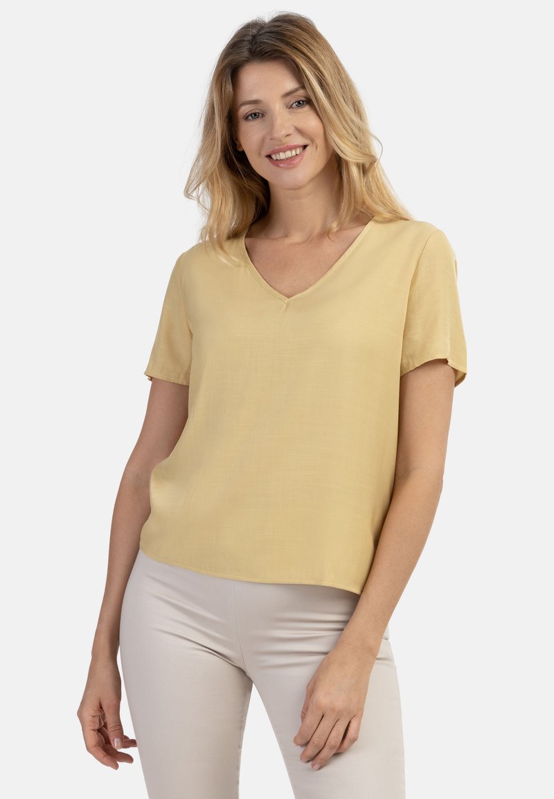 Kortærmet bluse med v-hals i lys gul, lavet af et glat stof med løs pasform, der har en lige kant og minimal dekor.