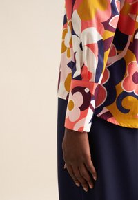 Blusa colorata con motivo floreale nelle tonalità di rosa, giallo e blu navy. Tessuto di cotone con dettaglio a bottoni sui polsini.