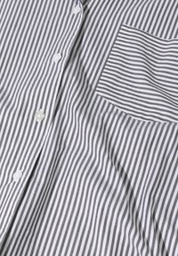 Chemise boutonnée avec des rayures verticales grises et blanches, comportant une poche poitrine gauche, un tissu lisse et des boutons blancs.