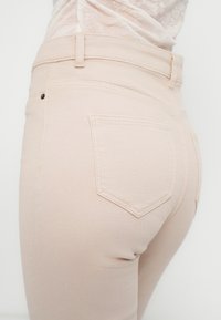 Ροζ τζήν με απαλό ύφασμα, με μεσαία μέση, πίσω τσέπες με ραφές και μικρό μαύρο κουμπί ως διακοσμητικό.