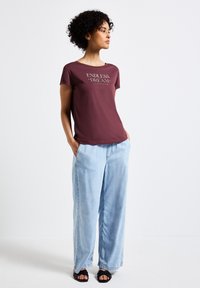 Burgundské bavlněné tričko s nápisem "ENDLESS DREAM", spárované s světle modrými širokými džínami a černými sandály. Casual střih a uvolněný design.