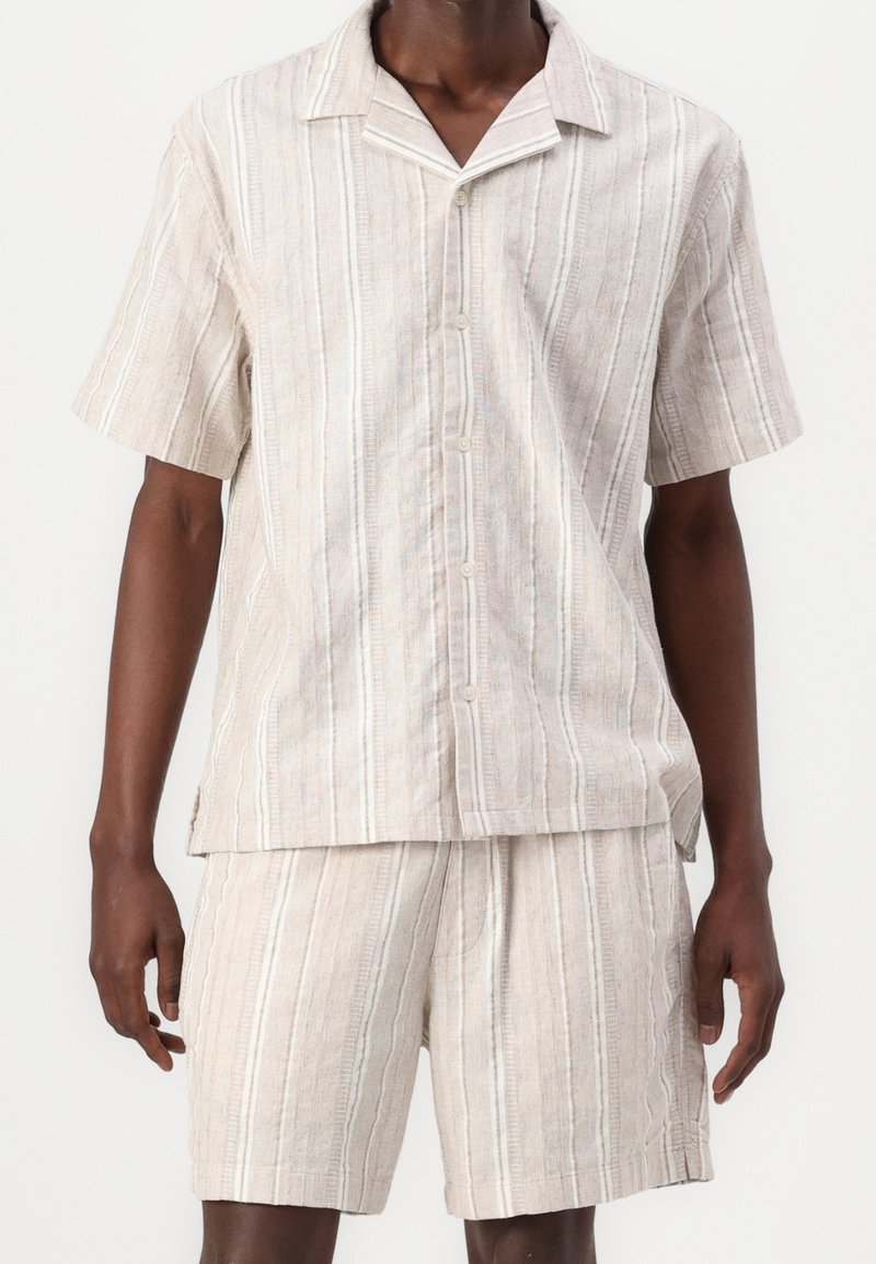 Camisa de manga corta de lino y pantalones cortos a juego en color beige claro con rayas verticales. Cuenta con cuello de solapa y cierre de botones. Tejido texturizado.