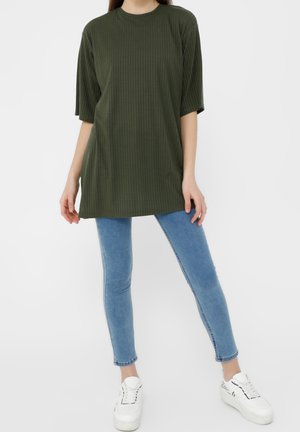 T-shirt oversize en rib en vert foncé avec des manches courtes, associé à un jean skinny bleu clair et des baskets blanches. Design simple et décontracté.