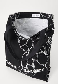 Borsa tote in tessuto nero con motivo lineare astratto bianco, caratterizzata da un ampio interno e doppi manici. Logo "SAMSØE" sul davanti.