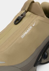 Sapatilha Nike Air Max bege com fecho de correr, lingueta de malha e almofada Air Max visível na sola.