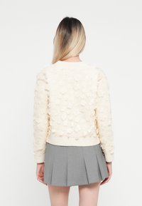 Maglione crema con decorazioni floreali texture, polsini e orlo a coste. Abbinato a una mini gonna plissettata grigia.