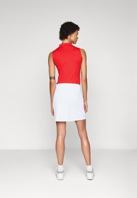 Red sleeveless polo top paired with a white skirt. The outfit features a fitted design and smooth fabric, worn with white sports shoes.
