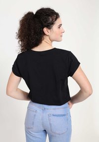 Černé, krátké tričko s krátkým rukávem a kulatým výstřihem, spojené se světle modrými kalhotami s vysokým pasem, které mají uvolněný střih.