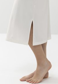 Robe blanche mi-longue avec fentes sur les côtés, fabriquée en tissu doux. Présente une texture simple et lisse ainsi qu'une coupe droite à l'ourlet.