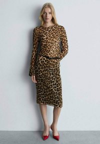 Leopardenmuster-Kleid mit langen Ärmeln, taillierter Silhouette und einem schwarzen Gürtel; kombiniert mit roten Spitzenabsatzschuhen. Glatte Stofftextur.