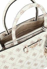 Witte Guess-handtas met beige logopatroon, dubbele handvatten, merkplaatje in goudkleur en een hoofdvak met ritssluiting.