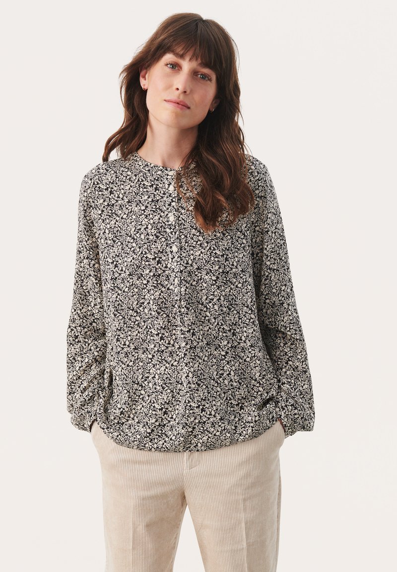 Zwart-wit bloemen blouse met knopen en lange mouwen en ronde halslijn, gemaakt van lichte stof, gedragen met beige corduroy pants.