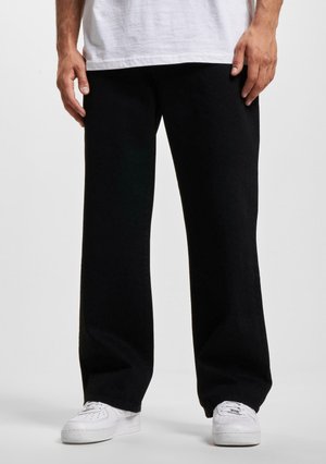Black wide-leg pants made of soft fabric with a smooth texture. Worn with white sneakers, displaying a relaxed fit and clean lines.