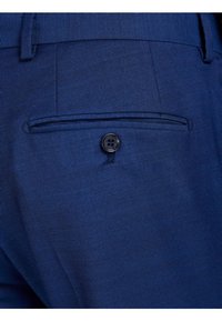 Navy blue fabric pants close-up, featuring a back pocket with a single black button and a smooth, textured surface.