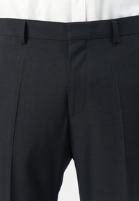 Dark gray plaid dress pants with front pleats and belt loops, worn with a white tucked-in shirt.