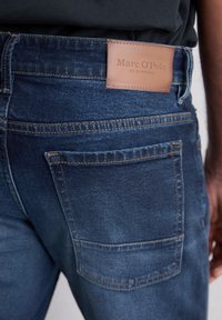 Donkerblauwe denim jeans met een leren label met de tekst "Marc O'Polo" op de achterkant. Voorzien van achterzakken en contraststiksel.