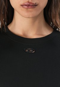 Black t-shirt with a round neckline, featuring a textured logo patch at the collar and a smooth fabric finish.