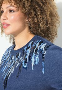 Sweatshirt bleu marine avec des ornements en sequins dans des nuances de bleu et de noir, présentant un col rond et un tissu texturé.
