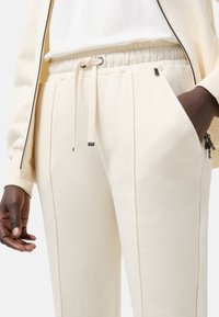 Crème-kleurige joggerbroek met een elastische tailleband, trekkoordsluiting, zijzakken en verticale stikdetails. Zachte stoftextuur.