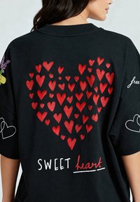 Črna bombažna majica s velikim rdečim srčnim motivom, sestavljenim iz manjših src, z besedilom "SWEET heart" in dodatnimi srčnimi grafikami.