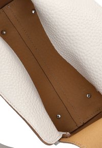 Witte textuur leren interieur van een tas, met een gladde tan voering. Zilverkleurige hardware zichtbaar nabij de randen.