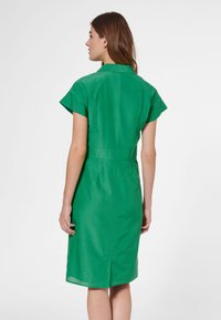 Grünes Kurzarmkleid mit einem kragenartigen Hals, taillierter Taille und knielangem Saum. Glattes Material mit einem einzelnen Rückenschlitz.