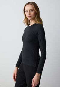 Schwarzes Langarmoberteil mit Rundhalsausschnitt, tailliertem Schnitt und leicht geschwungenem Saum. Hergestellt aus einem glatten, elastischen Stoff, der sich gut zum Schichten eignet.