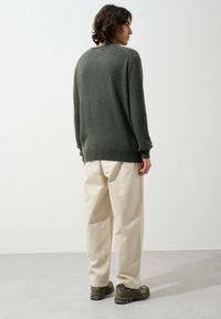 Grüner Wollpullover mit rundem Halsausschnitt, lockerer Passform und gerippten Bündchen, kombiniert mit beigefarbenen, weiten Hosen und dunklen Sneakers.