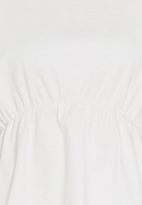 Robe blanche en coton avec une couture froncée à la taille, une texture lisse et un design simple. Le tissu est doux et léger.