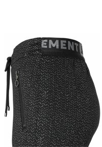 Närbild av svarta sportbyxor med grå zigzag-mönster, ficka med dragkedja på sidan och elastisk midja med delvis grå text.