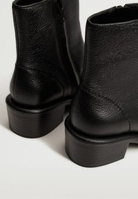 Bottes cheville en cuir noir à finition texturée, dotées d'une fermeture éclair latérale et d'un talon épais et strié pour une stabilité accrue.