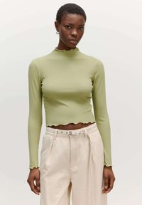 Lichtgroene geribbelde lange mouwen top met een opstaande kraag en golvende onderrand, gecombineerd met crèmekleurige hoge taille broeken met een knoopdetail.
