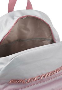 Una mochila gris con una cremallera rosa, que cuenta con un interior espacioso con una textura similar a la satén y un logotipo bordado en rosa claro en la parte frontal.