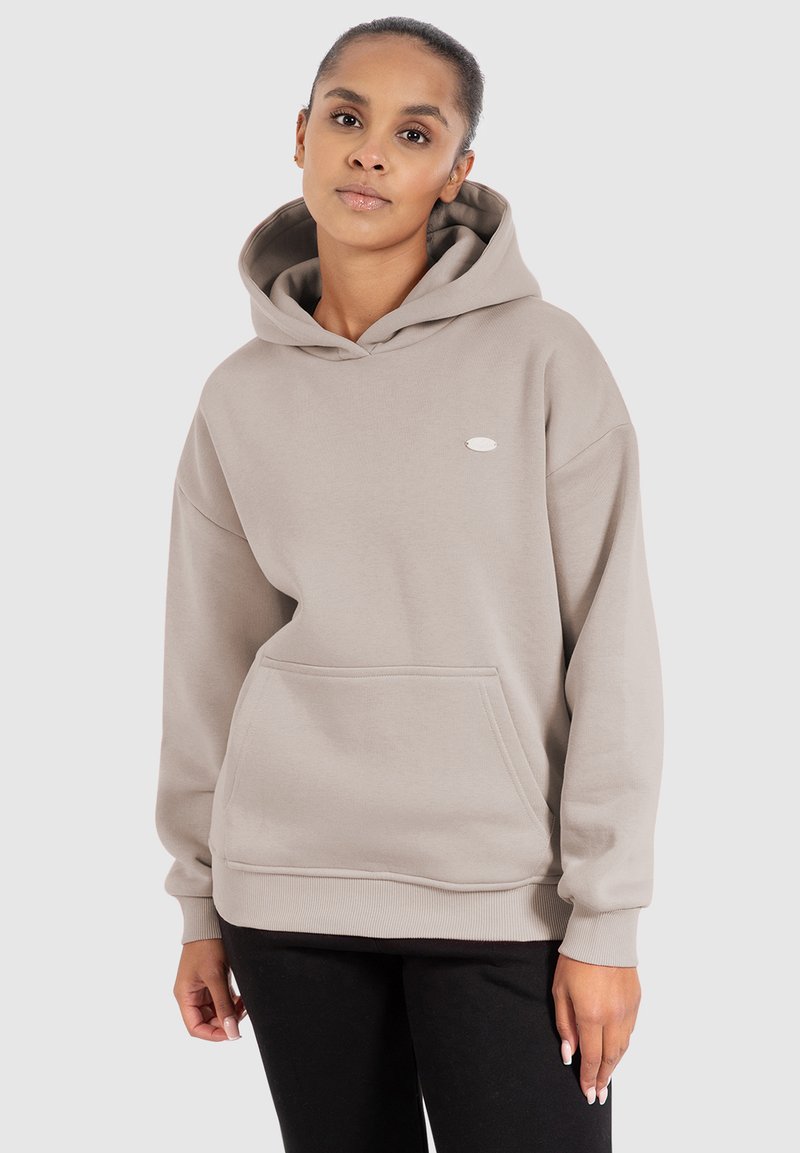 Haut à capuche beige clair avec une poche avant, un cordon de serrage au niveau de la capuche et un logo discret sur la poitrine. Fabriqué en tissu doux et texturé. Coupe décontractée.