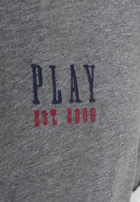 Tela gris con el texto bordado "PLAY" en azul marino y "EST. 2006" en hilo rojo.