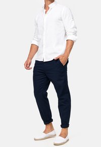 Camisa blanca de lino con botones, pantalones tapered en azul marino y zapatos blancos de slip-on. El conjunto tiene un ajuste relajado y las mangas dobladas.