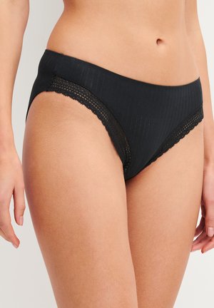 Zwarte geribde bikini-onderbroek met kanten rand gedragen door een persoon, die de onderkant van de romp en de bovenkant van de dijen toont tegen een effen achtergrond.