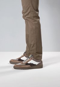 Zapatillas de piel vuelta marrón y cuero blanco de caña baja con detalles texturizados, suelas de goma y cordones a contraste, combinadas con pantalones beige.